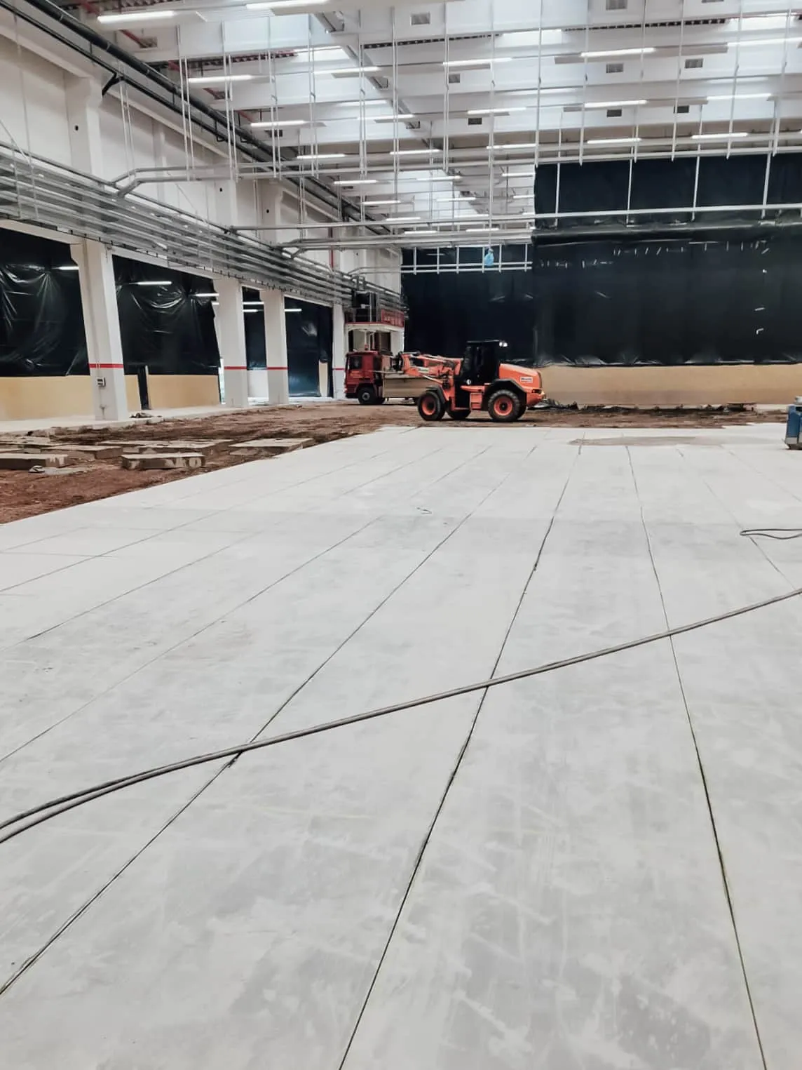 Großer Hallenboden mit herausgetrenntem Betonfeld, im Hintergrund eine Baumaschine